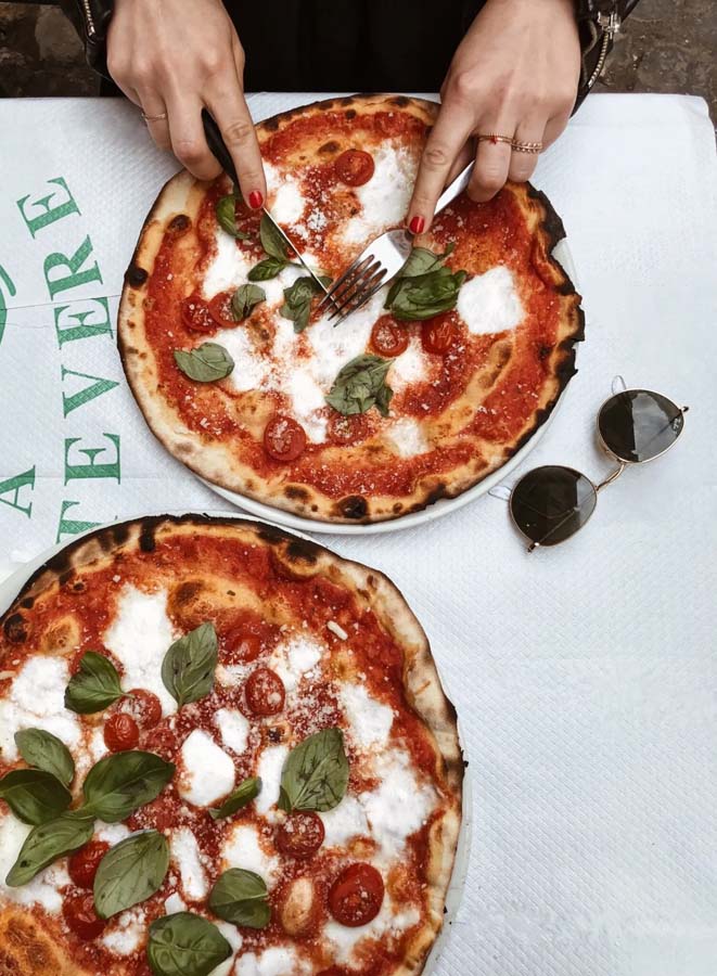 Woman’s hands cutting a pizza with tomato sauce, mozzarella, basil and fresh tomatoes