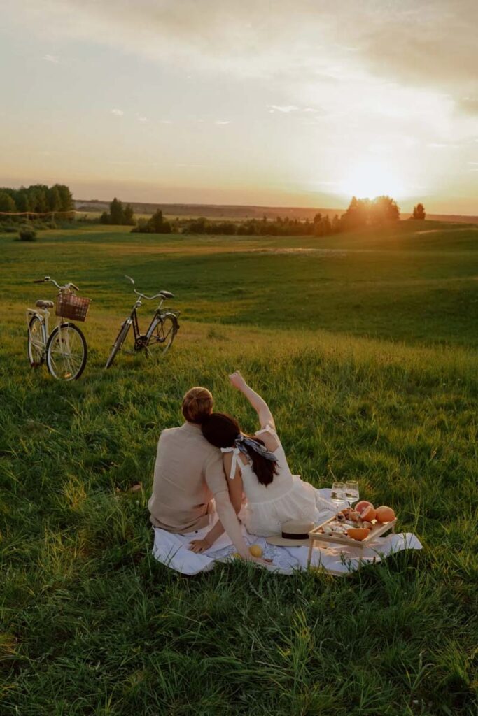 Couple having a picnic in a green field looking at sunset